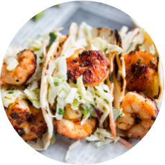 Grilled shrimp tacos topped with shredded cabbage and white sauce in soft tortillas.