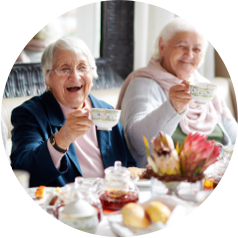 Two senior women enjoy a cheerful tea time together with pastries and flowers on the table.