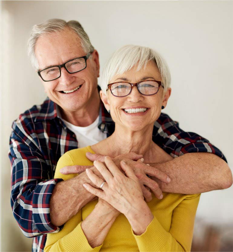 Elderly couple smiling with glasses in an affectionate embrace.