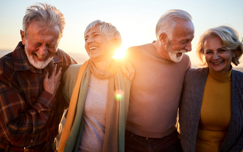 Happy group of senior friends laughing together outdoors at sunset.