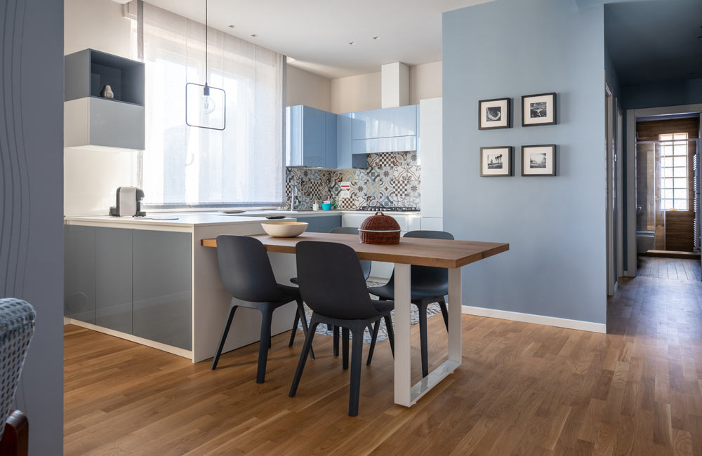 Modern kitchen with light blue cabinets and wooden dining area.