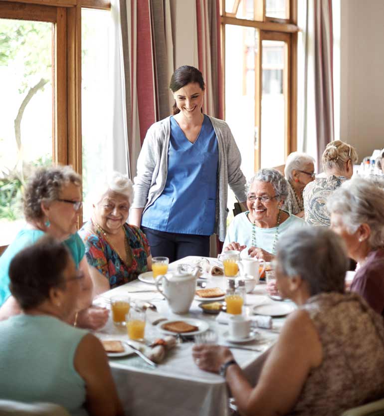 Group of seniors dining together with a caregiver in an assisted living facility.