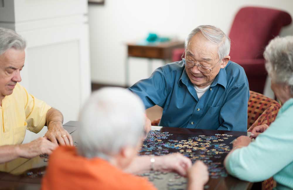 Group of senior friends working together on a jigsaw puzzle at a table in a cozy room.