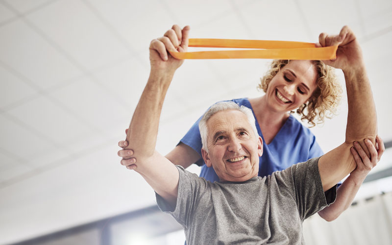 Senior man exercising with resistance band assisted by healthcare professional in a wellness center.