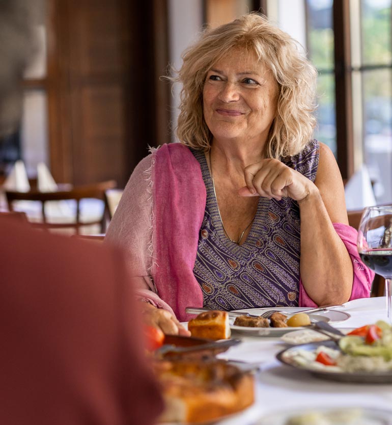Senior woman enjoying a meal with friends at a restaurant, smiling and looking engaged.