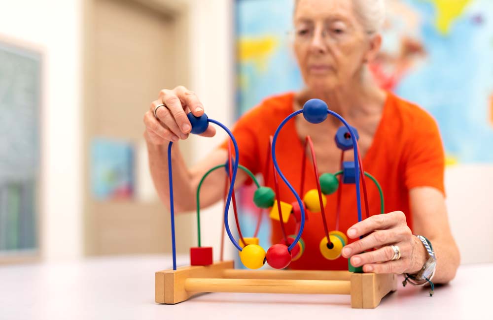 Senior woman engages in memory care activity using colorful beads and wires in a calming environment.