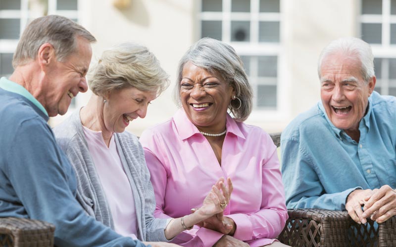 Four senior individuals laughing and enjoying each other’s company outdoors in a courtyard.