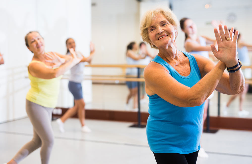 Seniors participating in an active dance class at a fitness studio, following the instructors moves.